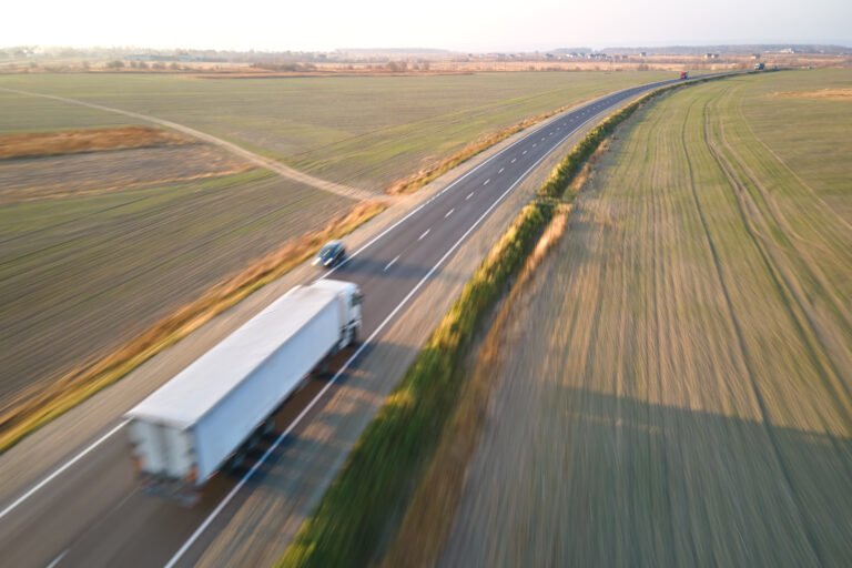 Aerial view of blurred fast moving semi-truck with cargo trailer driving on highway hauling goods in evening