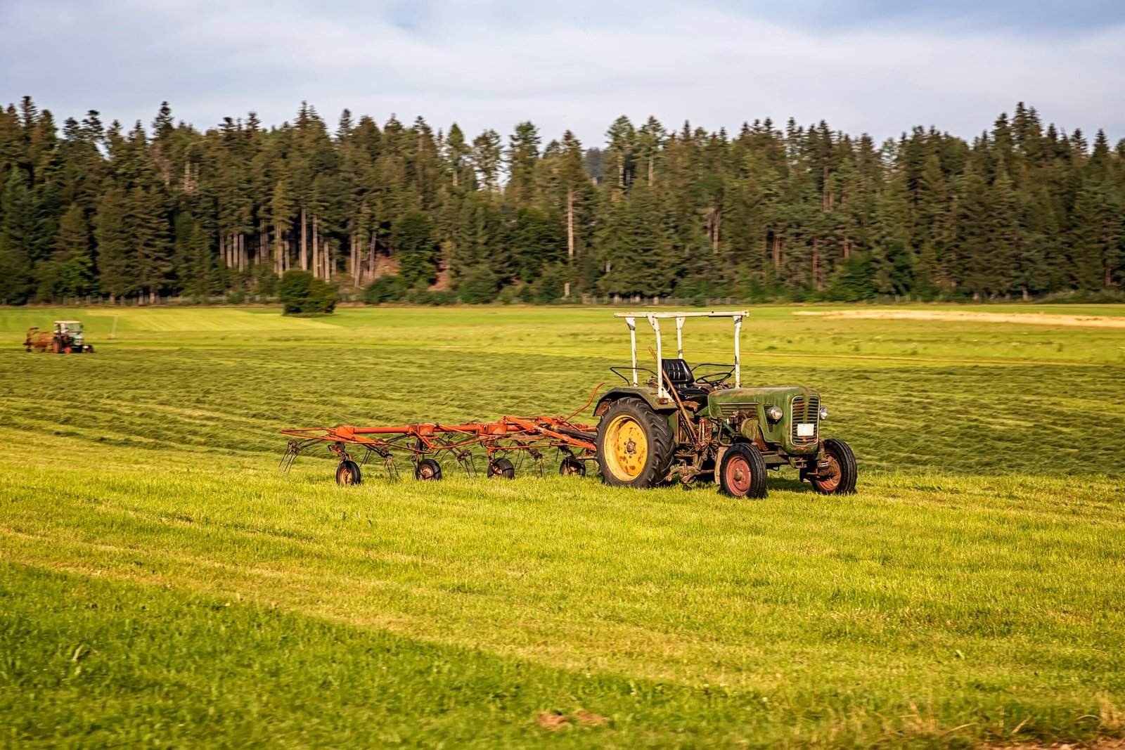 Agricultural machinery, a tractor collecting grass in a field ag